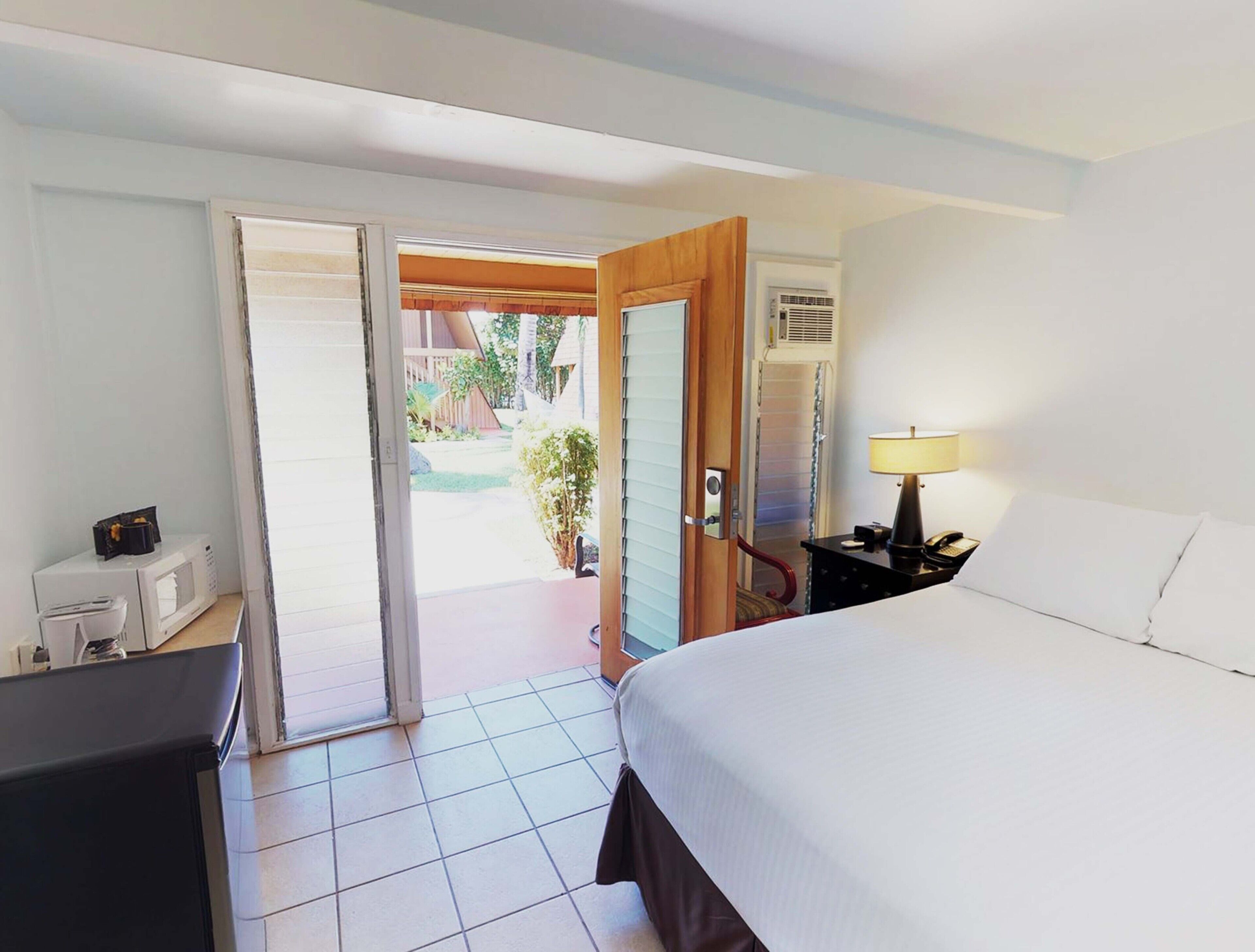 Une chambre d’hôtel comprenant un lit, un bureau avec une lampe, une chaise et une porte coulissante donnant sur un balcon.