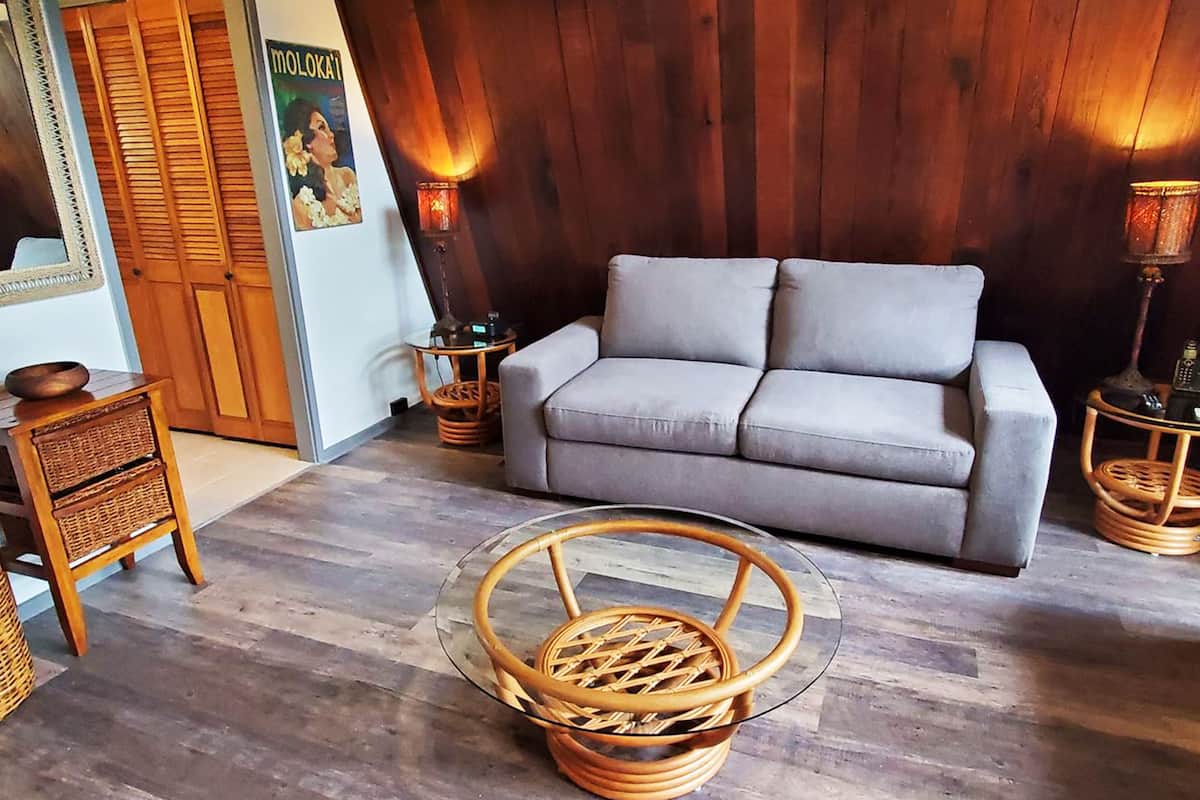 Ein Wohnzimmer mit grauem Sofa, Korbstühlen-Nebenischen und einem Glastisch.