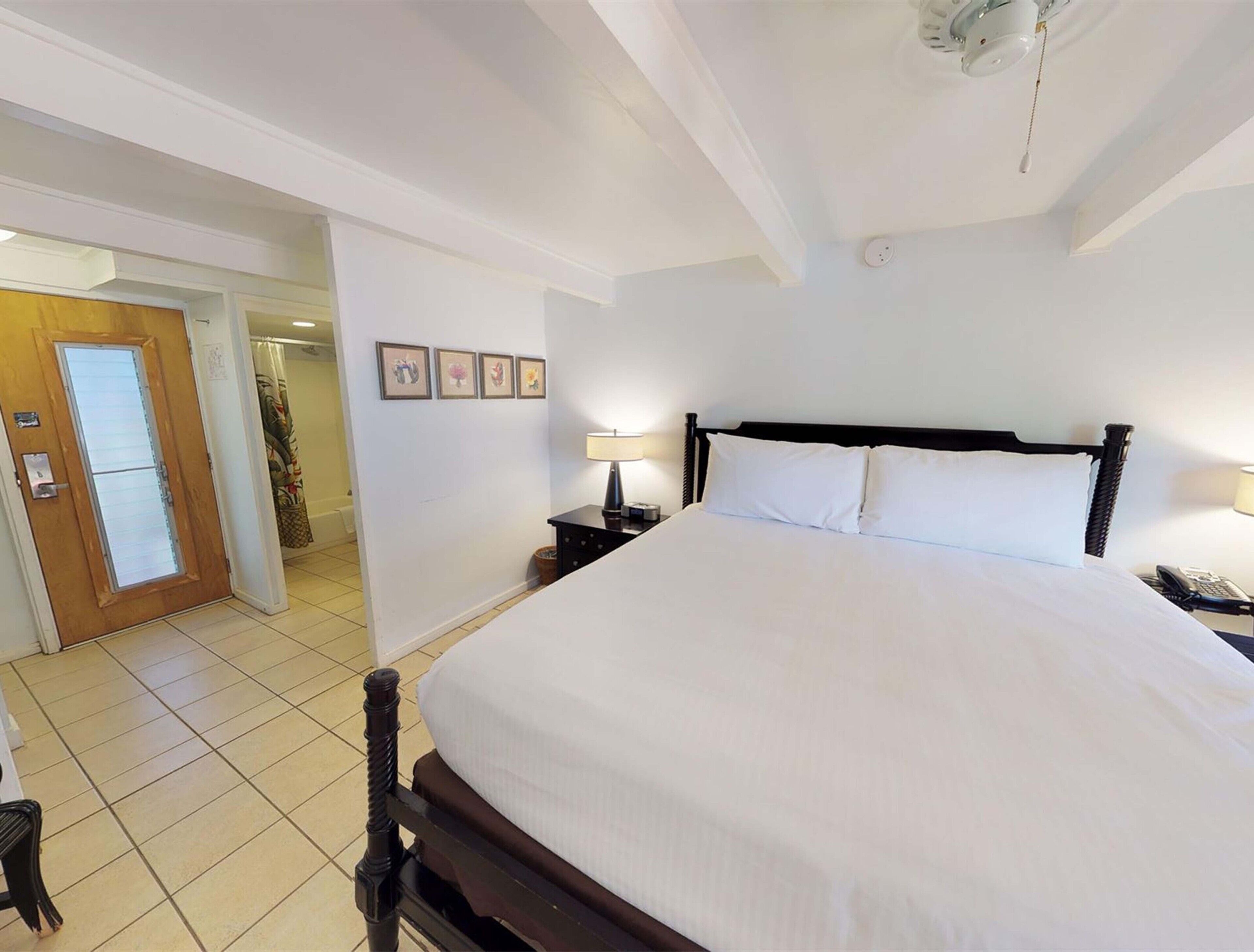 Een hotelkamer met een groot bed, een houten hoofdbord, een nachtkastje met een lamp en een deur naar een badkamer.