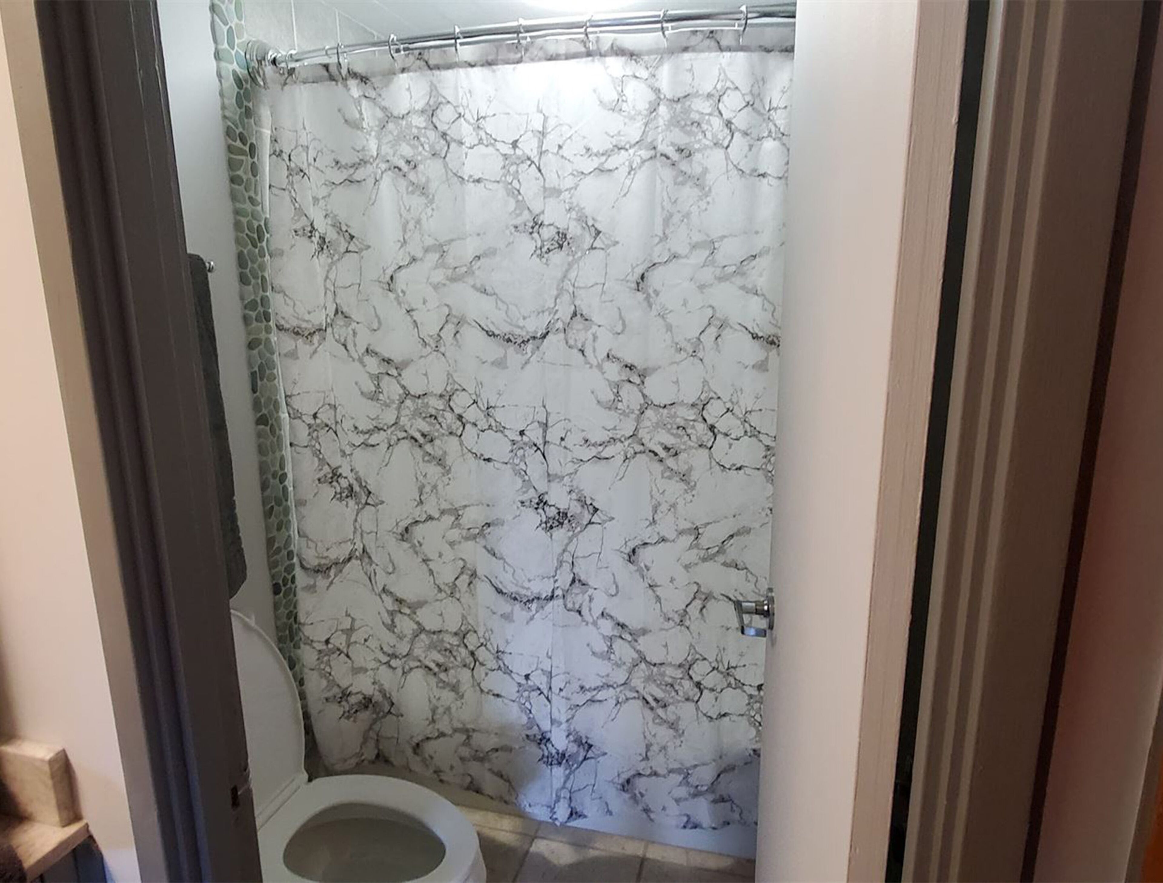 A bathroom with a marble-patterned shower curtain, a toilet, and a tiled floor.