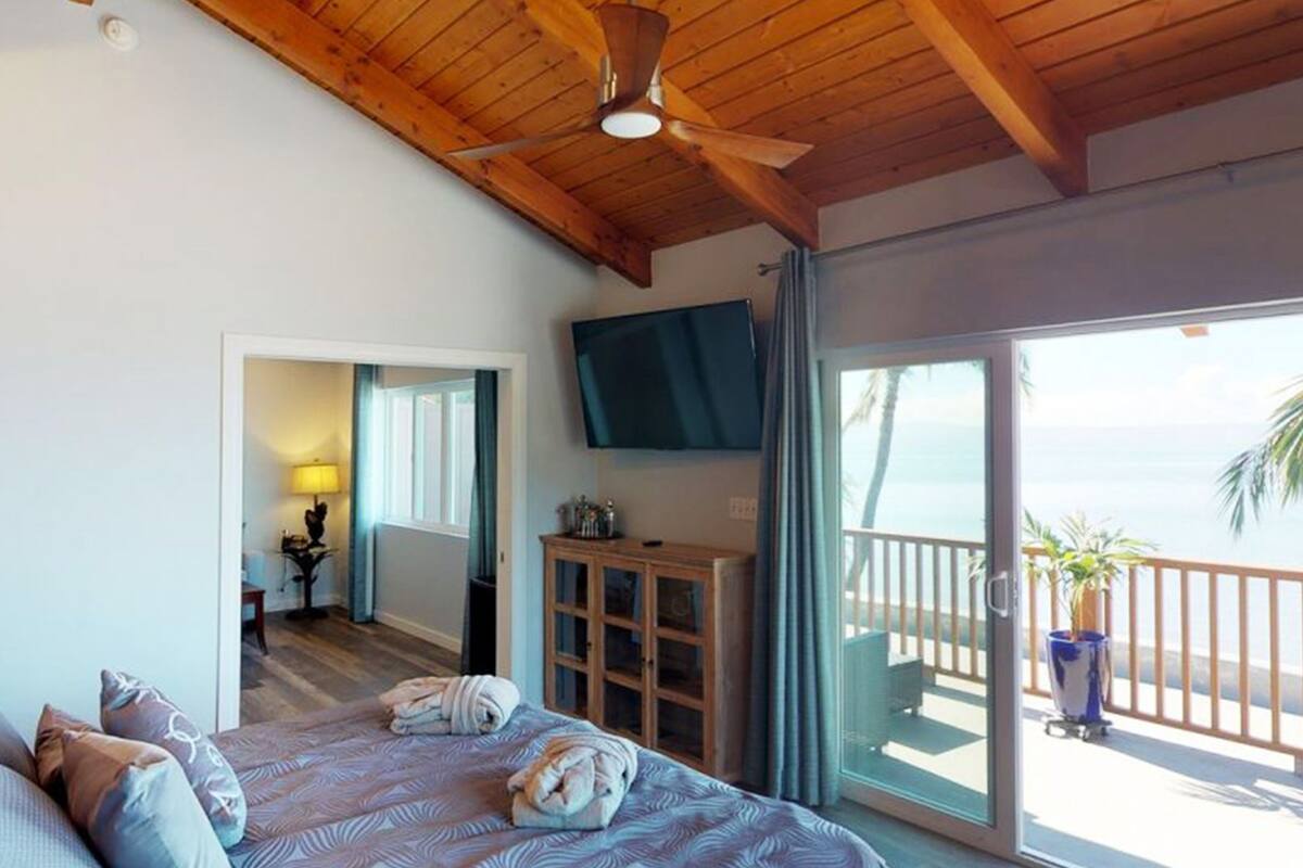 Ein Schlafzimmer mit einem großen Bett, einem Deckenventilator, einem Fernseher und einem Balkon mit Meerblick.