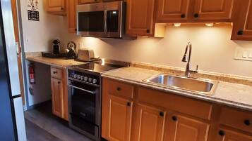 Una cocina con armarios de madera, un lavamanos de acero inoxidable, un microondas, un tostador y un horno.