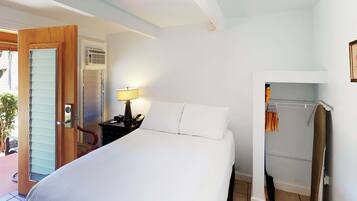A hotel room with a bed, a bedside table with a lamp, a telephone, and a coat rack with clothes.