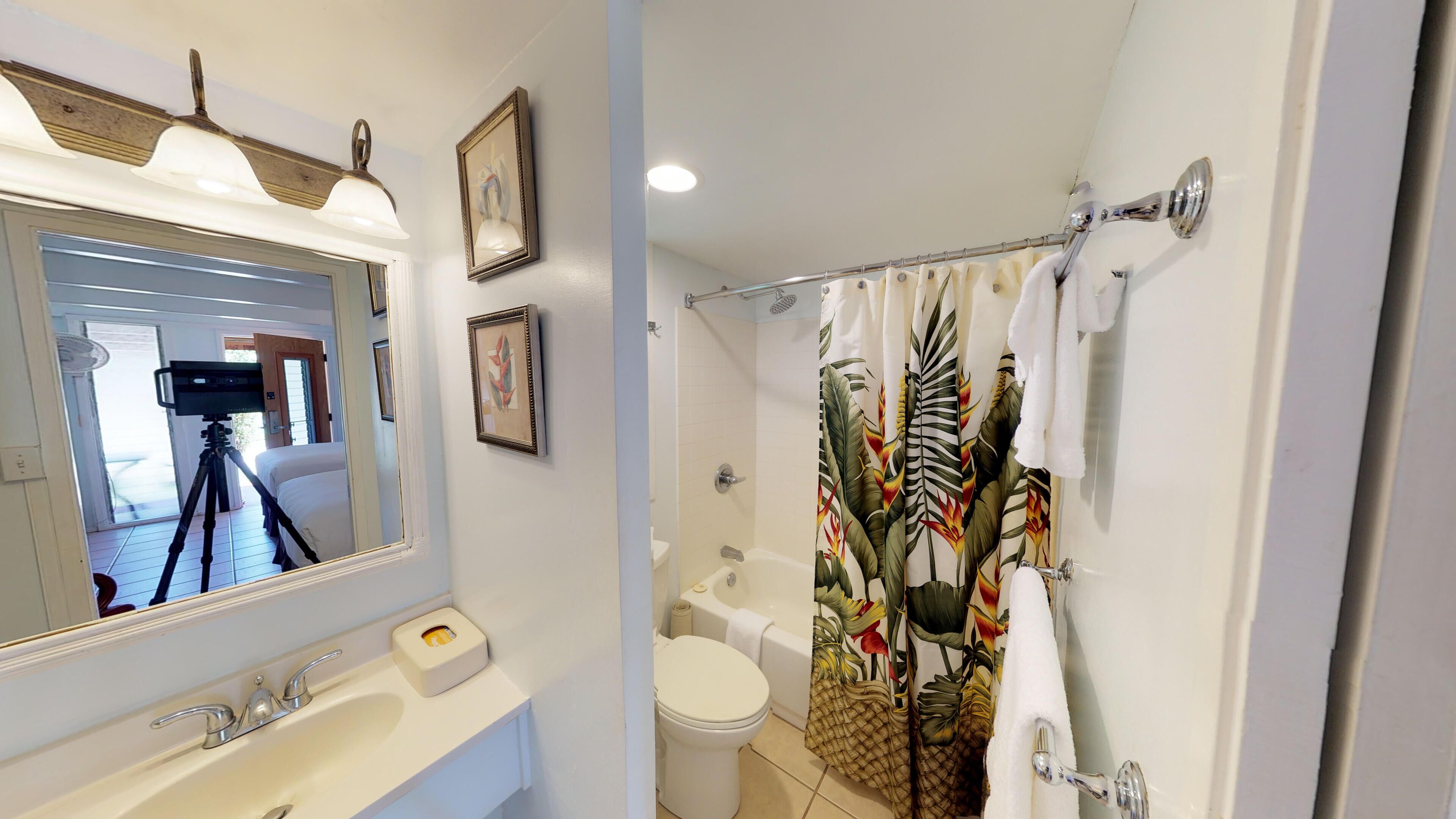 A bathroom with a bathtub, toilet, sink, and a shower curtain with a tropical leaf pattern.
