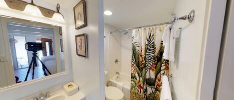 Un baño con bañera, inodoro, lavamanos y cortina de ducha con estampado de hojas tropicales.