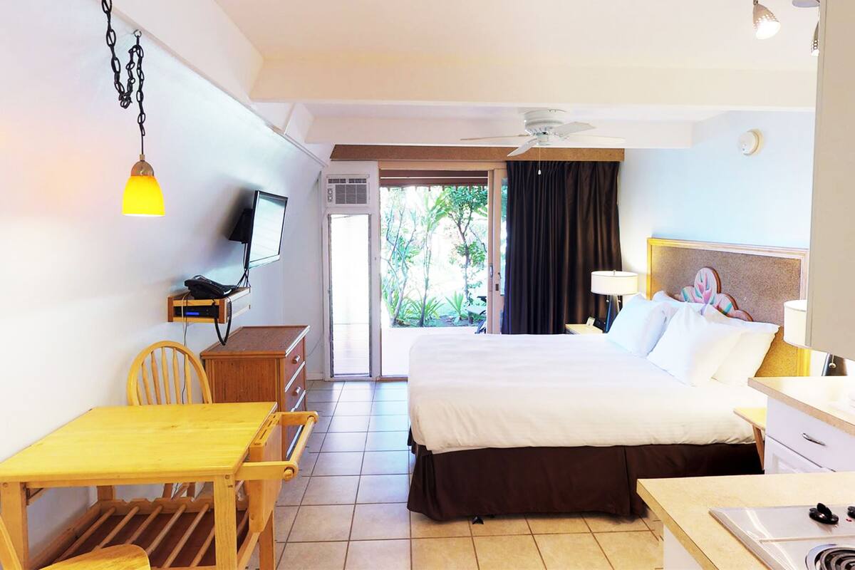 Ein Hotelzimmer mit einem Bett, einem Schreibtisch mit Stuhl, einem Fernseher, einem Deckenventilator und Blick ins Freie.