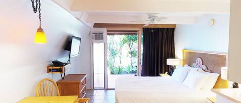 A hotel room with a bed, a desk with a chair, a television, a ceiling fan, and a view of the outdoors.