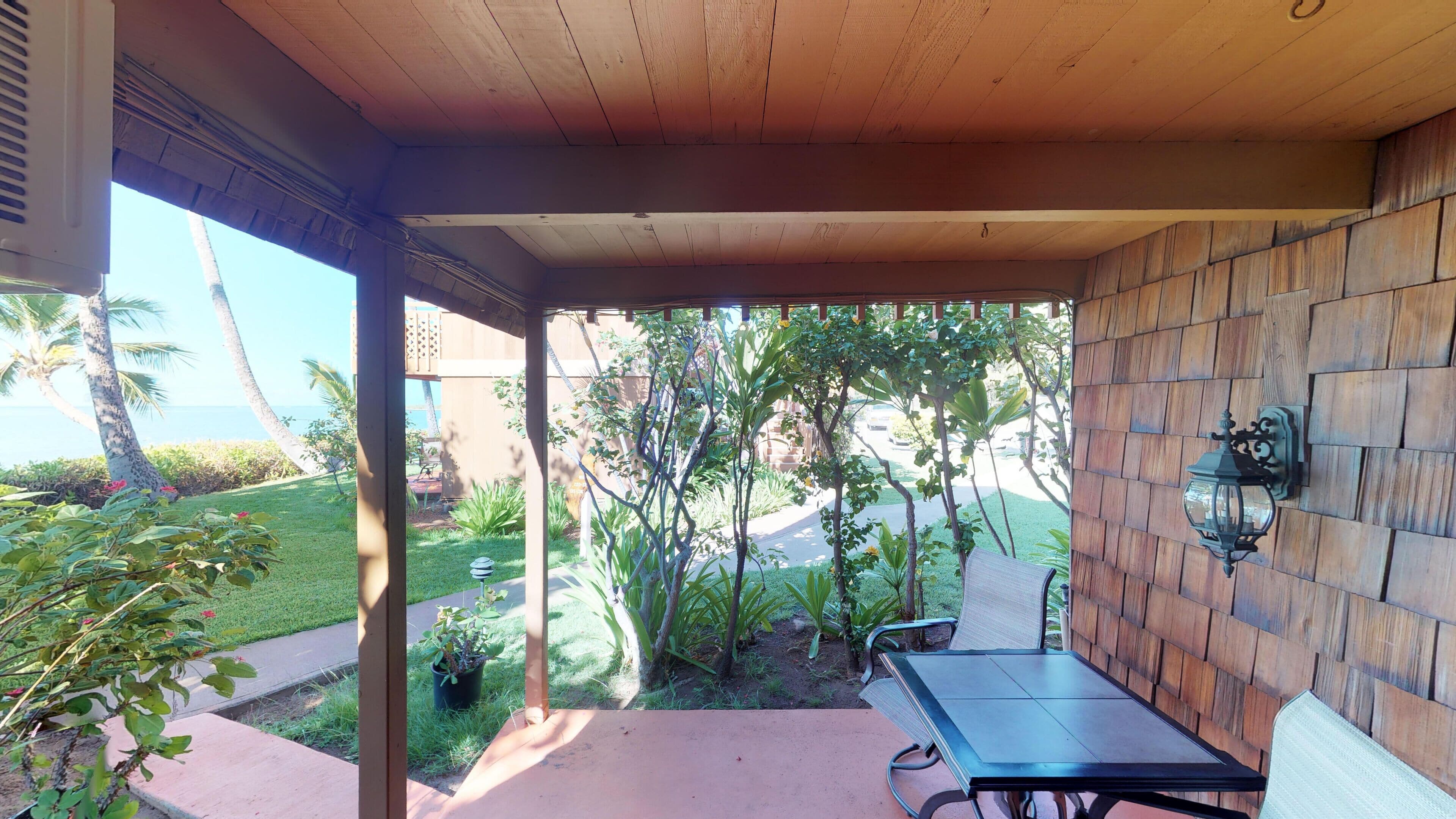 Un porche techado con una mesa y sillas, rodeado de paredes de madera y plantas en macetas.