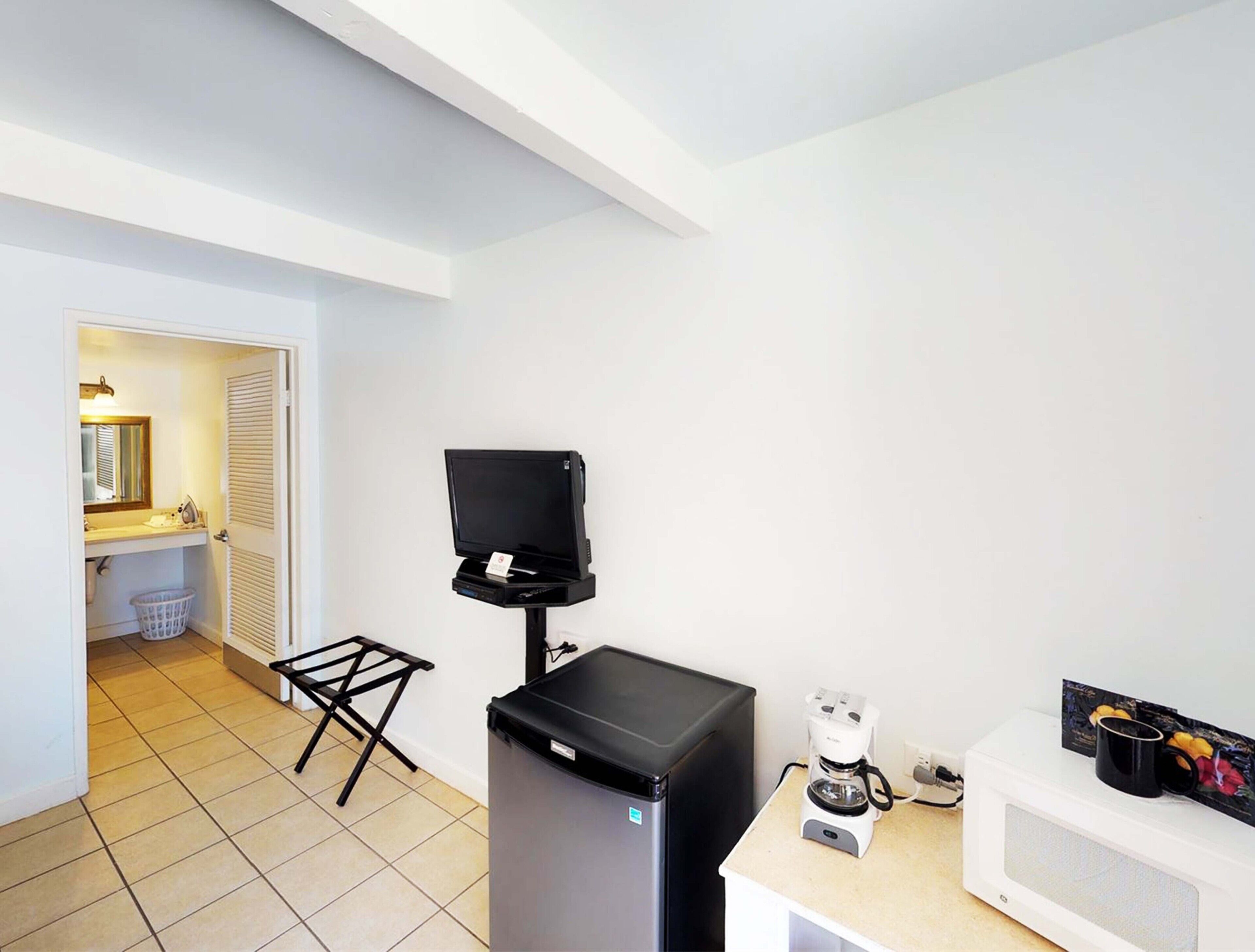 A compact kitchenette with a microwave, coffee maker, and a small TV on a stand.