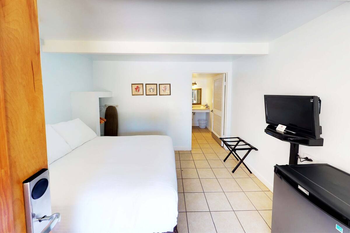 Ein Hotelzimmer mit Bett, Fernseher, Schreibtisch und einem durchgegangenen Tür erkennbaren Badezimmer.
