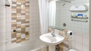 Un baño con bañera, lavabo e inodoro. Hay toallas y artículos de aseo en estantes.