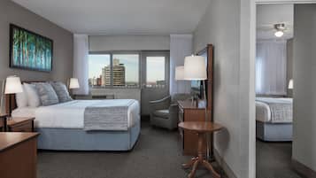 A hotel room with a bed, two bedside tables, a chair, a small round table, a mirror, and a view of the cityscape through the window.