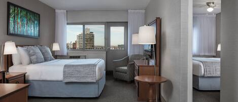 A hotel room with a bed, two bedside tables, a chair, a small round table, a mirror, and a view of the cityscape through the window.