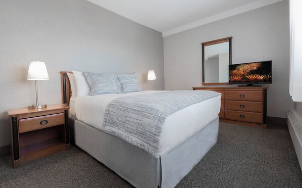 Une chambre d’hôtel comprenant un lit, des tables de chevet, une commode, un téléviseur et un miroir.