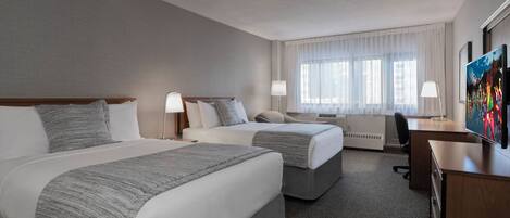 A hotel room with two beds, a desk, a chair, and a TV.