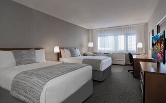 A hotel room with two beds, a desk, a chair, and a TV.