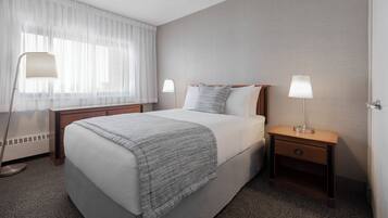 Une chambre d’hôtel avec un lit, deux tables de chevet avec des lampes, une fenêtre avec des rideaux légers et un ventilateur de plafond.