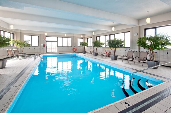 An indoor swimming pool with clear lanes, potted plants, and seating areas.