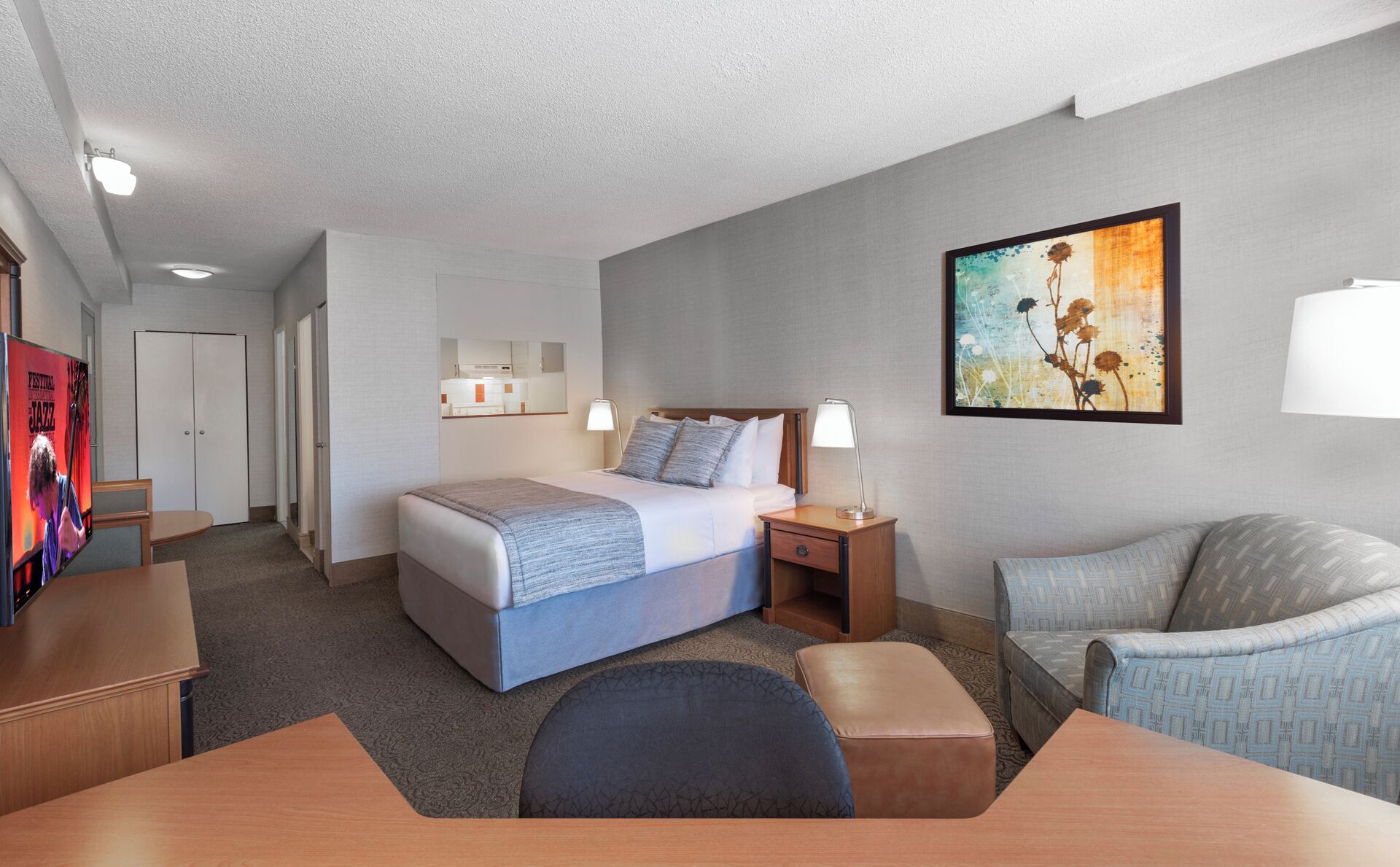 Una habitación de hotel con cama, mesitas de noche, escritorio, silla, sofá y un cuadro en la pared.