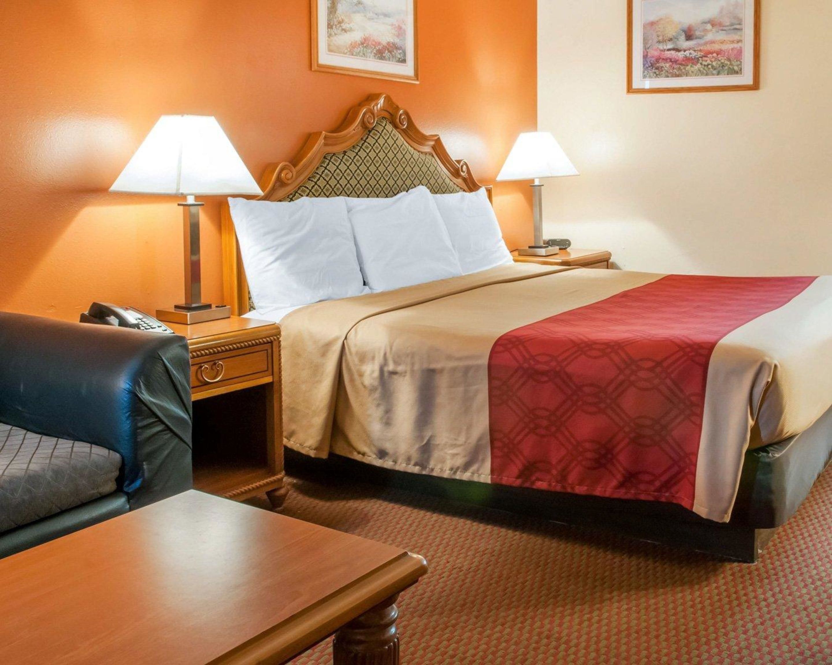 A hotel room with a bed, two bedside lamps, a telephone, a wooden nightstand, a leather armchair, and a wooden table.
