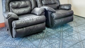 Two black leather recliner sofas with a footrest, positioned on a patterned tile floor. - Econo Lodge Hobbs (Hobbs)