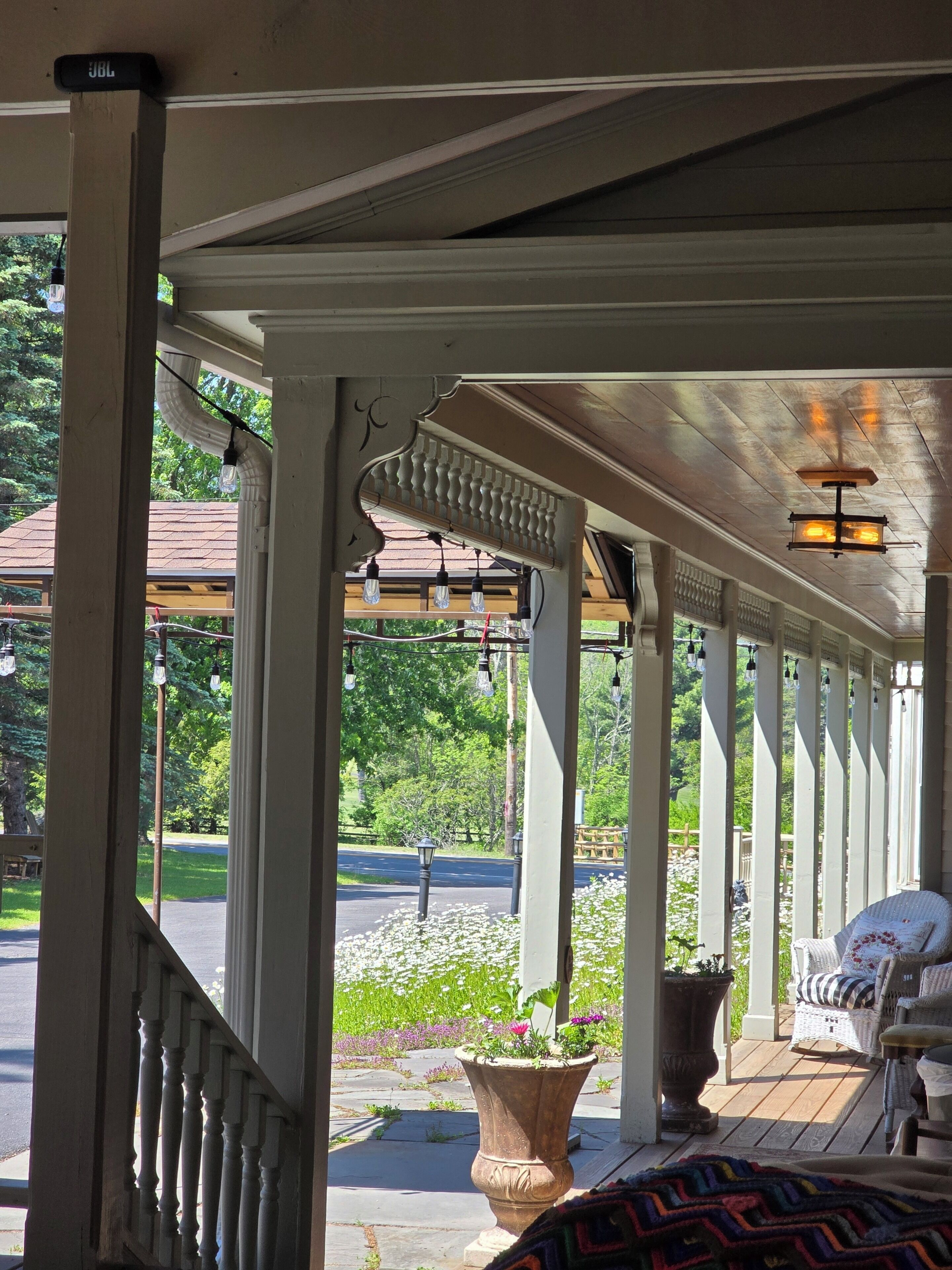 A covered porch with a railing, potted plants, and a wicker chair.