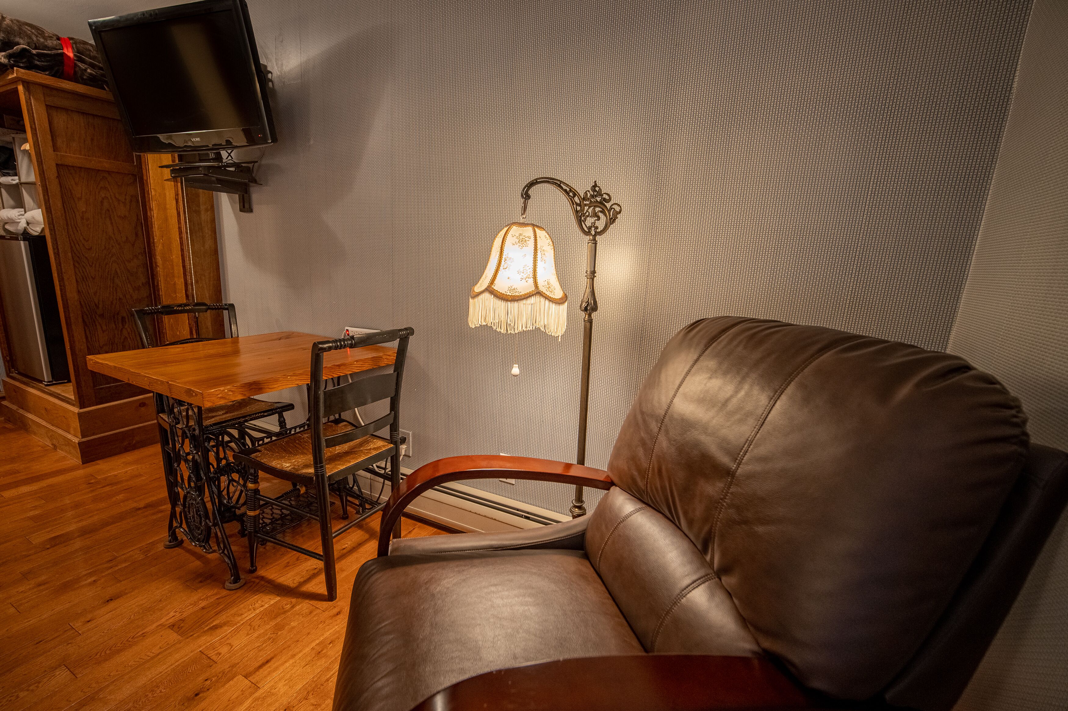 A living room with a wooden dining table, a leather sofa, a vintage lamp, and a mounted television.