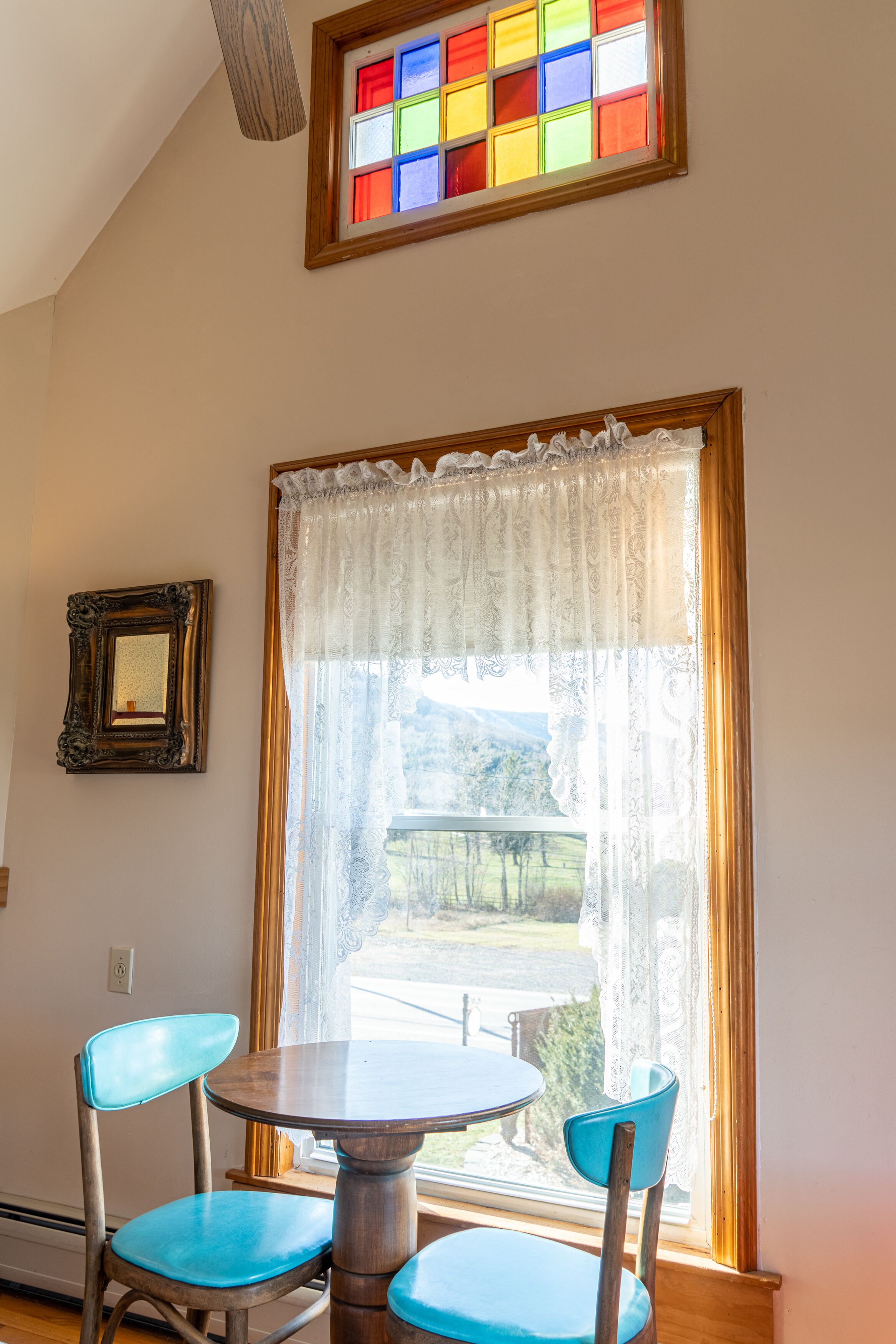 Ein Essbereich mit Tisch und zwei Stühlen, ein Fenster mit Blick ins Freie und ein gerahmtes Bild an der Wand.