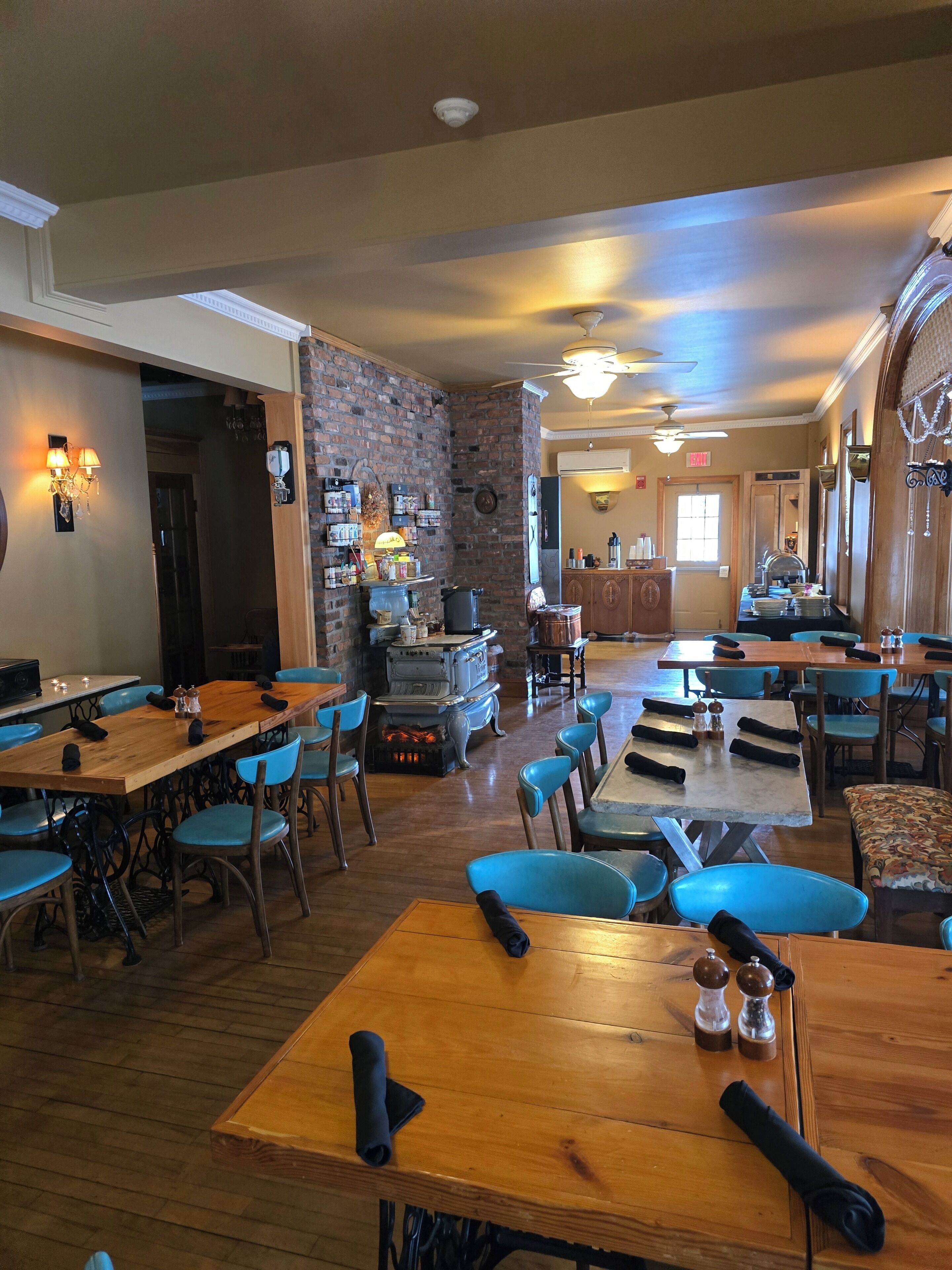 Un restaurant avec de nombreuses tables en bois et des chaises bleues, un mur en briques et un ventilateur de plafond.