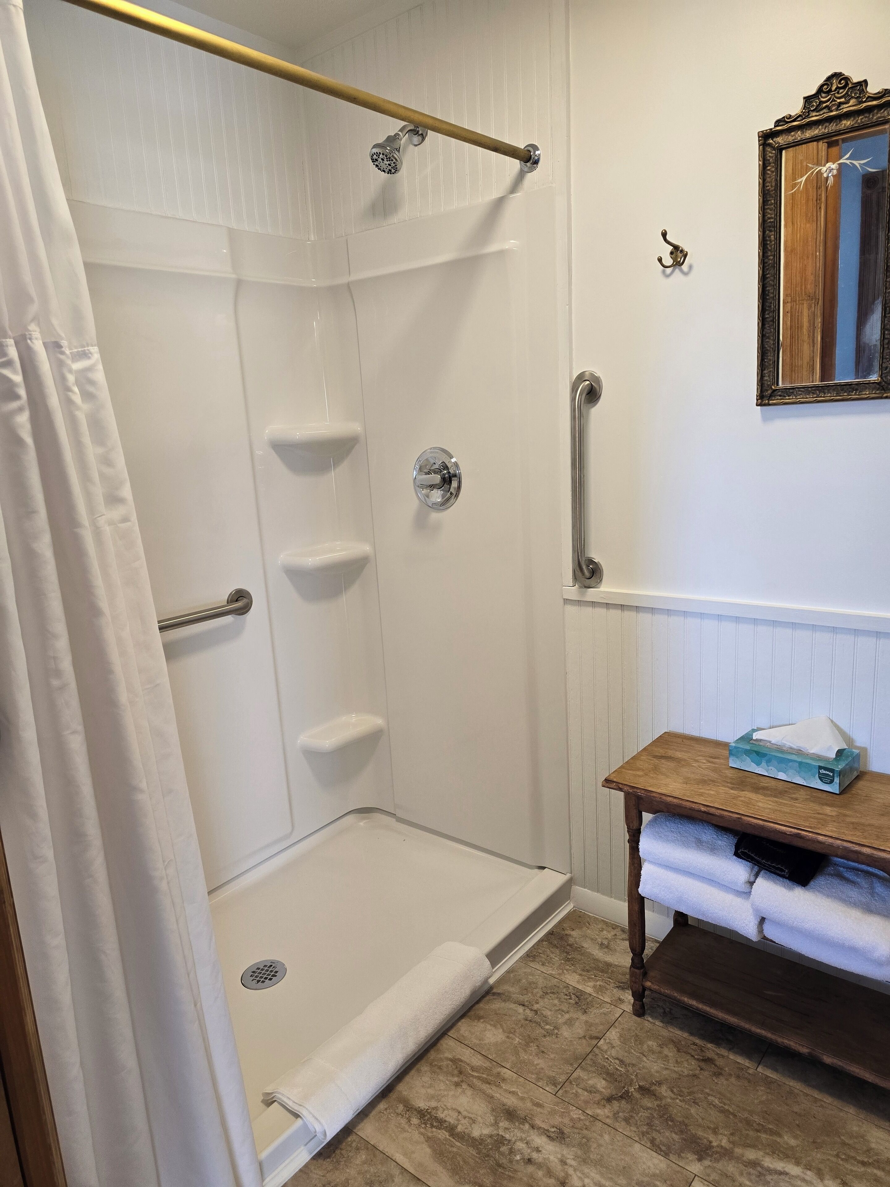 A bathroom with a walk-in shower, a wooden vanity with a towel rack, and a mirror on the wall.