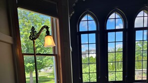 A room with a wooden floor, a chair, a lamp, and a view through a window with a decorative frame. - Albergo Allegria Hotel (Windham)