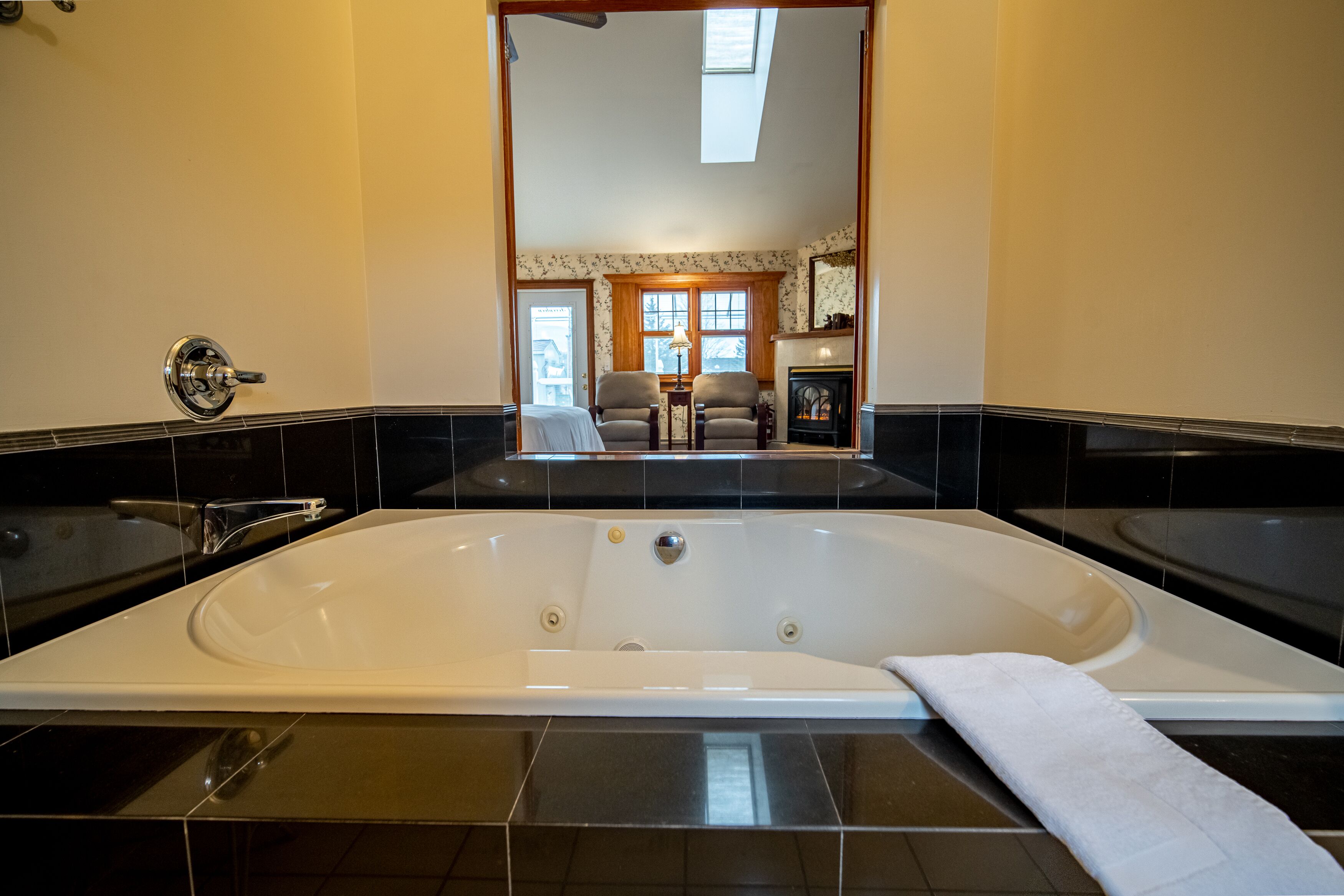 A modern bathroom with a large bathtub, a separate shower area, and a view of a living room through an open doorway.