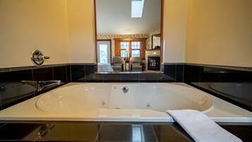 A modern bathroom with a large bathtub, a separate shower area, and a view of a living room through an open doorway.