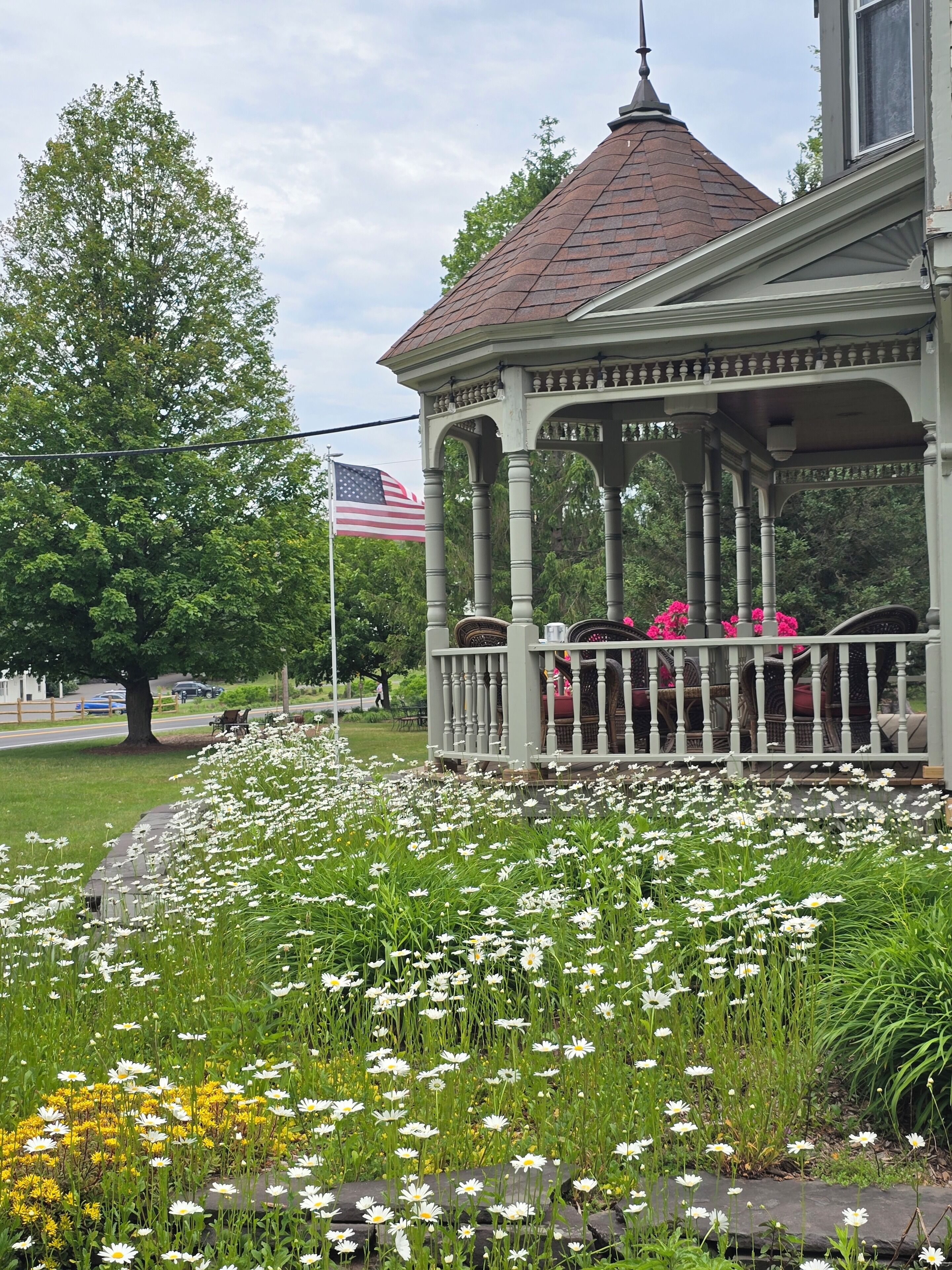 A gazebo with a tiled roof, surrounded by a garden with white and yellow flowers.