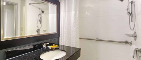 Un baño con lavabo de superficie negra, un espejo grande, ducha con cabezal de ducha manual y un perchero para toallas.
