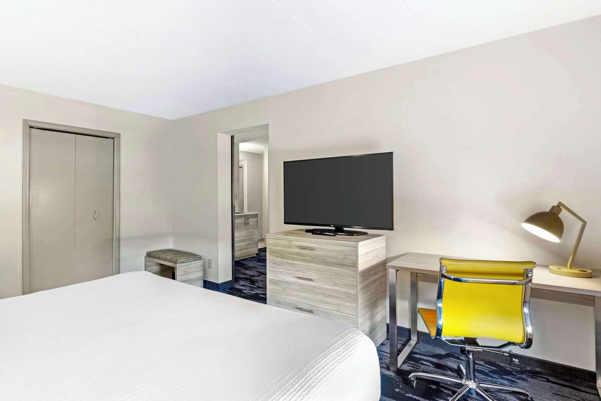 A hotel room with a bed, a TV, a desk with a chair, and a lamp.