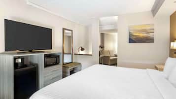 A modern hotel room with a large bed, a flat-screen TV, a microwave, a coffee maker, a seating area with a lamp, and a painting on the wall.