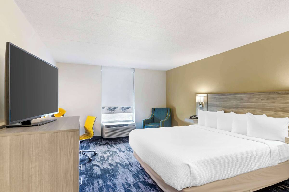 A hotel room with a large bed, a flat-screen TV, a desk, a chair, and a window with a view.