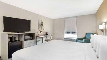 Une chambre d’hôtel avec un grand lit, un téléviseur à écran plat, un bureau avec une lampe, un four à micro-ondes et une chaise.