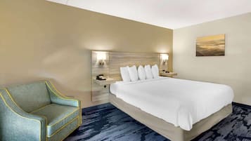 A hotel room with a bed, a sofa, a nightstand with a phone, and a painting on the wall.