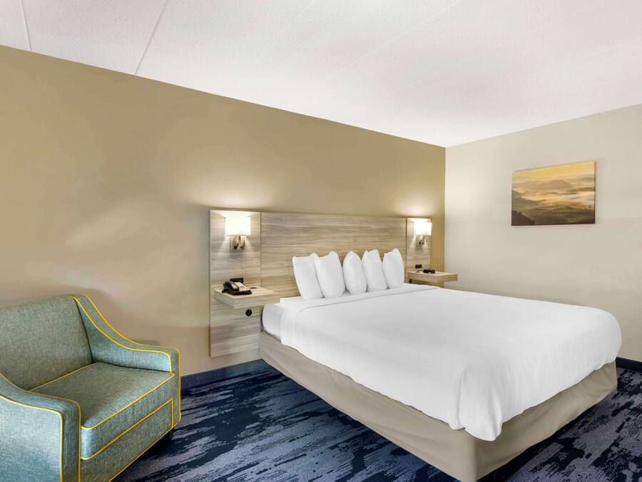 A hotel room with a bed, a sofa, a nightstand with a phone, and a painting on the wall.