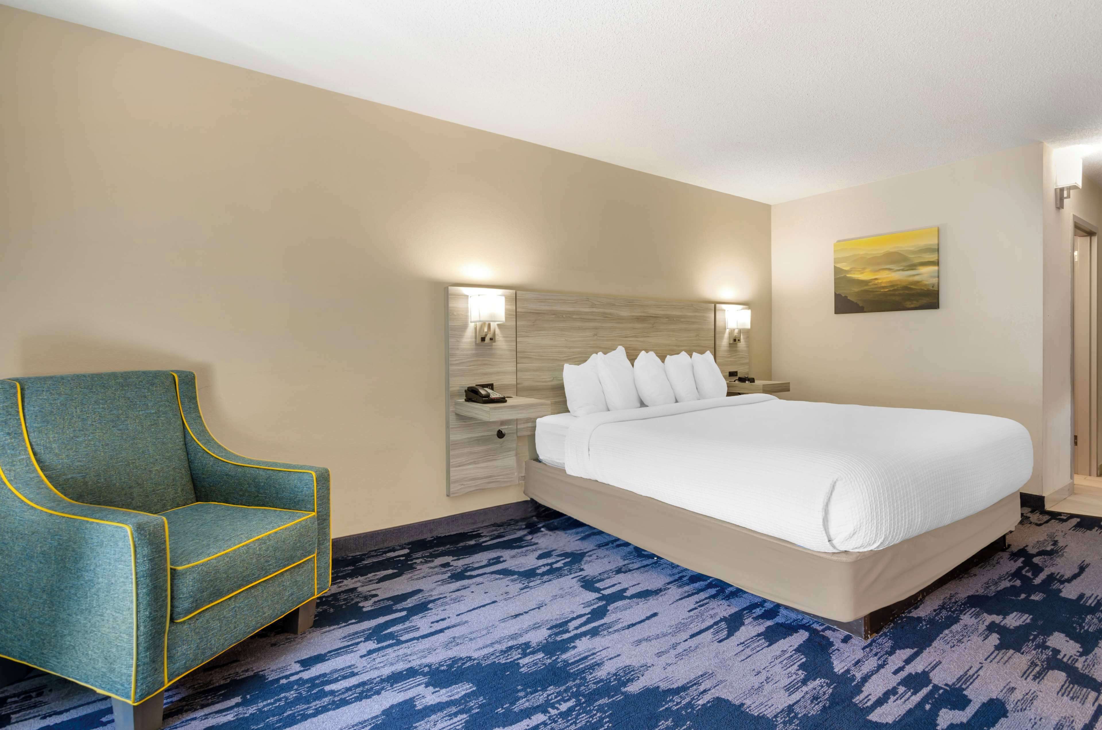 A hotel room with a large bed, a chair, a nightstand, and a wall-mounted lamp.