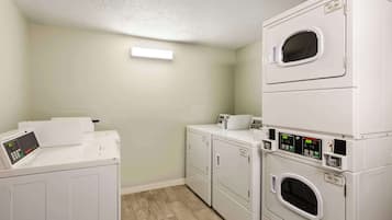 A laundry room with stacked washers and dryers, a control panel, and a light fixture.