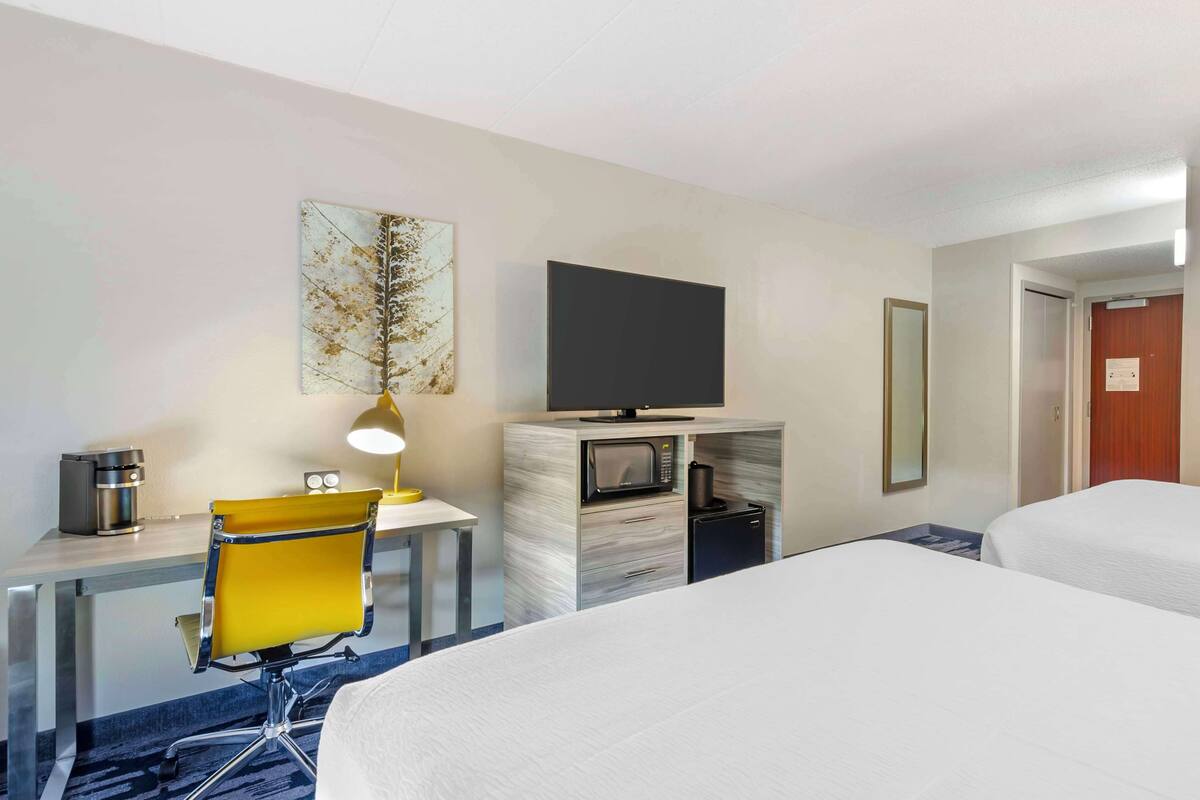 A hotel room with a bed, a desk with a chair, a television, a microwave, and a coffee maker.