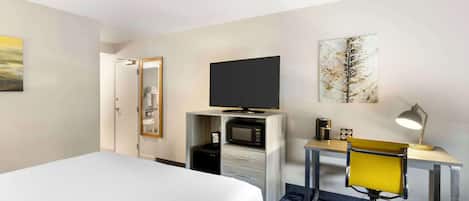 A hotel room with a bed, a desk with a chair, a television, a microwave, and a small cabinet.