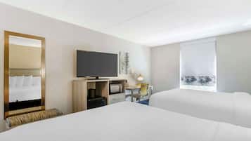 A hotel room with two beds, a television, a desk with a computer, a microwave, and a window with a view of trees.