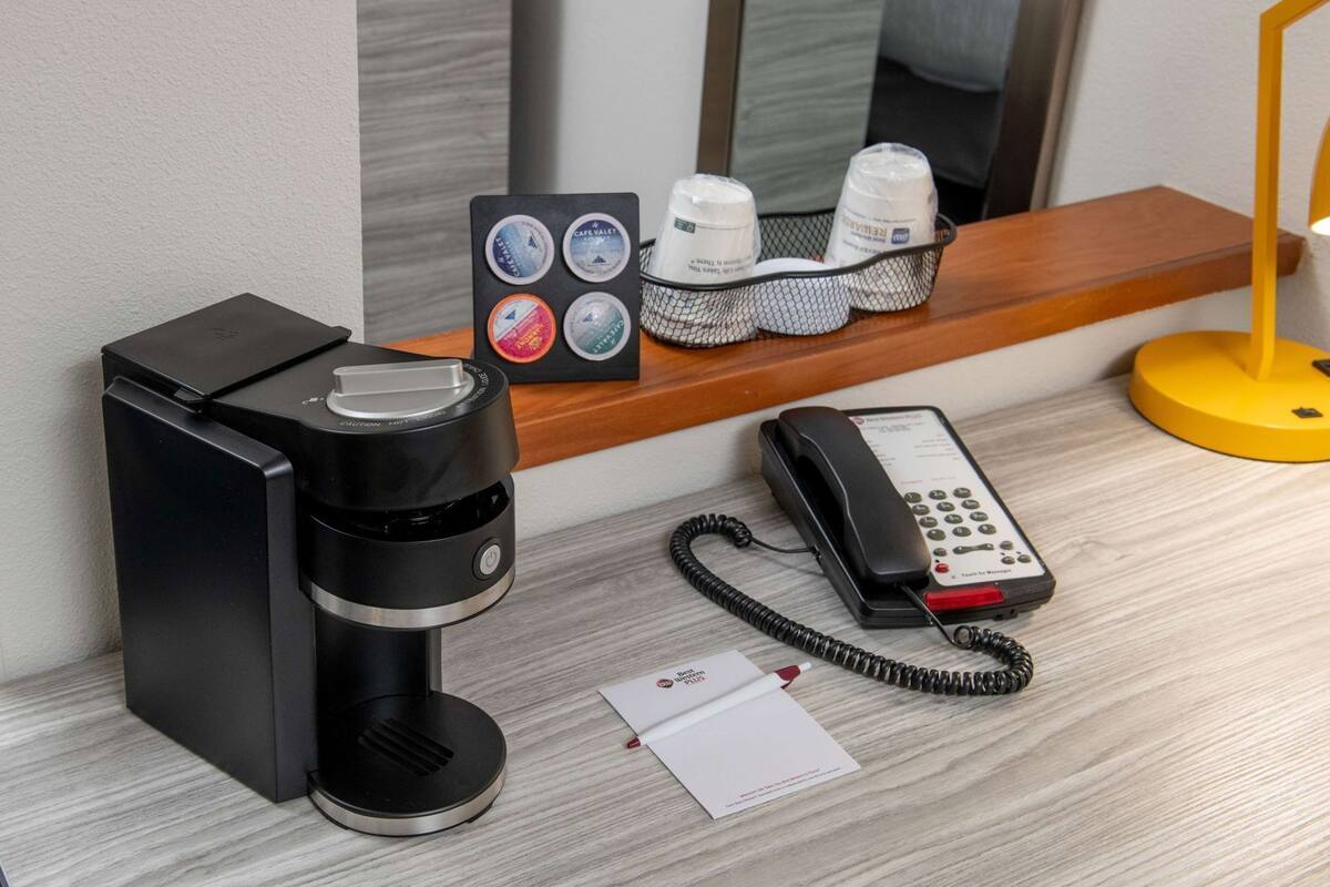 A coffee maker, a telephone, a tray with toiletries, and a mirror in a hotel room.