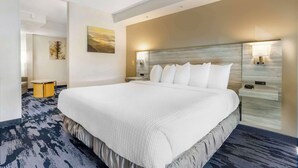 Una habitación de hotel moderna con una cama grande, una mesita de noche, una lámpara y una obra de arte colgada en la pared.