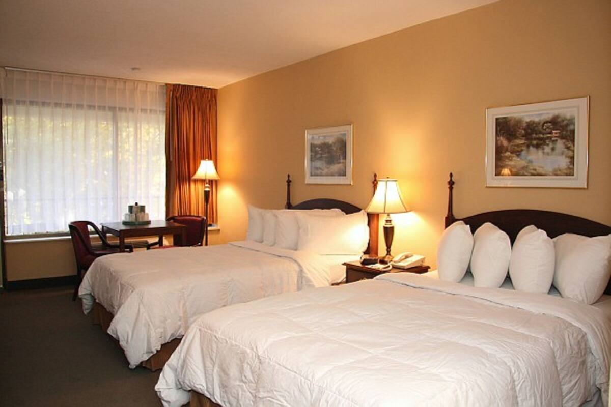 A hotel room with two beds, a desk, and a chair. There are two lamps on the nightstands and two framed pictures on the wall.