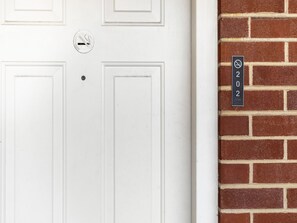 A white door with a no-smoking sign and a doorbell. A brick wall with a door number sign '202' is visible.